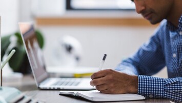 Man achter laptop schrijft in een notitieboek